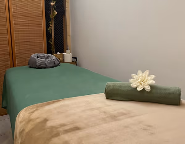 Massage table with a green sheet and a rolled towel with a white flower